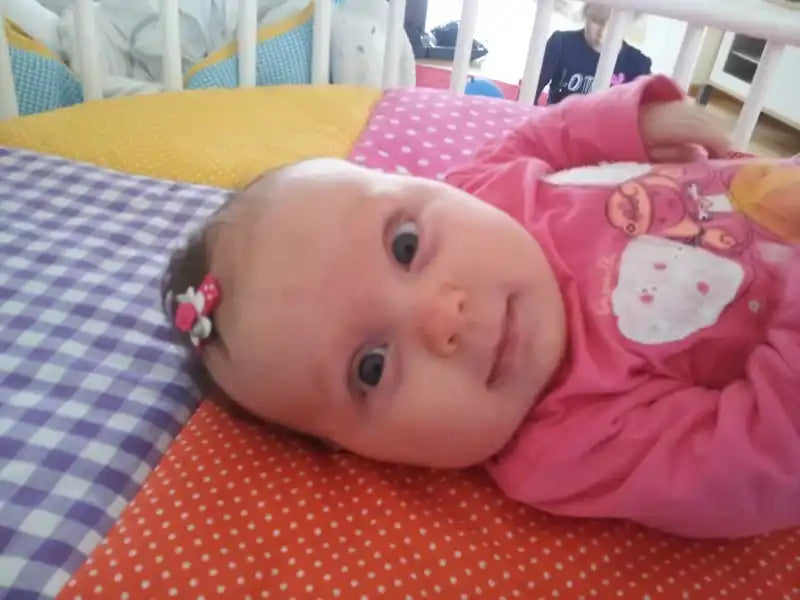 Een baby die een roze langmouwen top draagt met een decoratieve strik in haar haar.