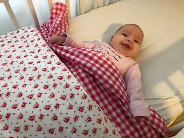 Een gelukkig baby in een wieg met een rood-wit geruit dekentje.