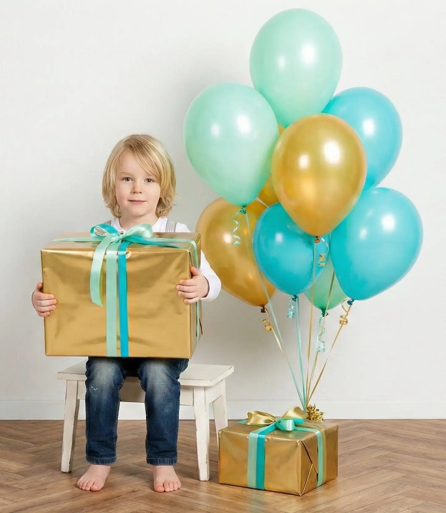 Een kind houdt een grote, goudverpakte cadeau-doos vast, vastgebonden met een turquoise lint.