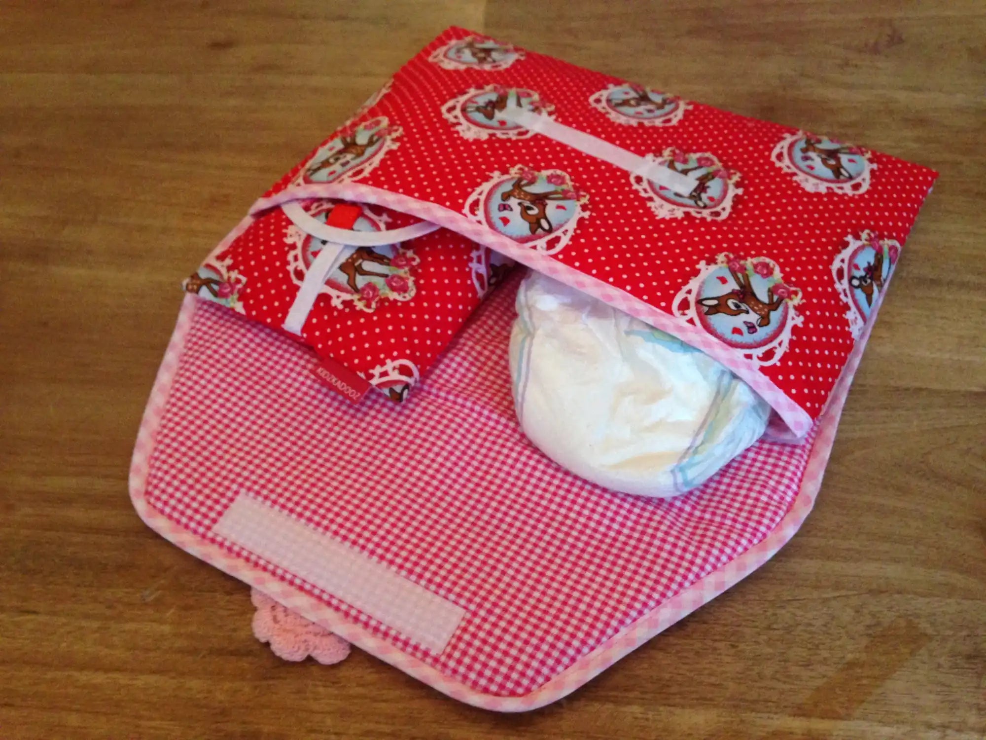 Een rood en roze met patroon luiertasje met een luier en doekjes.