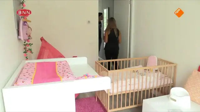 Roze en witte baby-ledikant met bloemmotief beddengoed, houten frame.