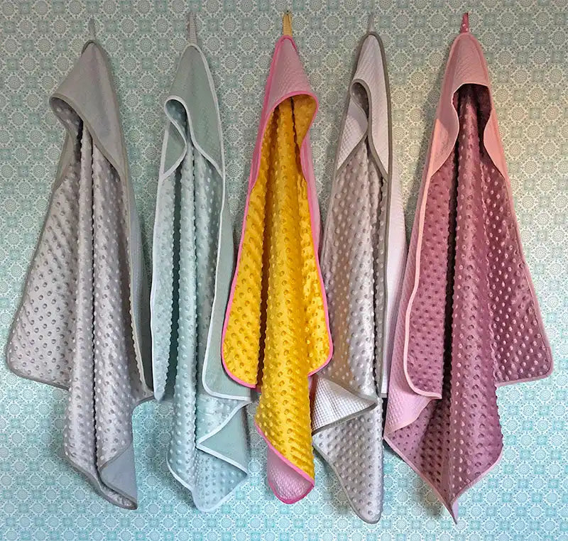 Vijf capuchonbabydekentjes in verschillende kleuren en texturen.