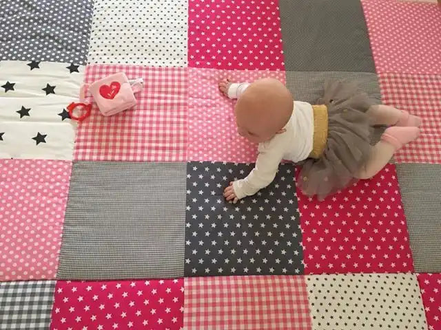 Een baby die op een patchwork speelmat kruipt.