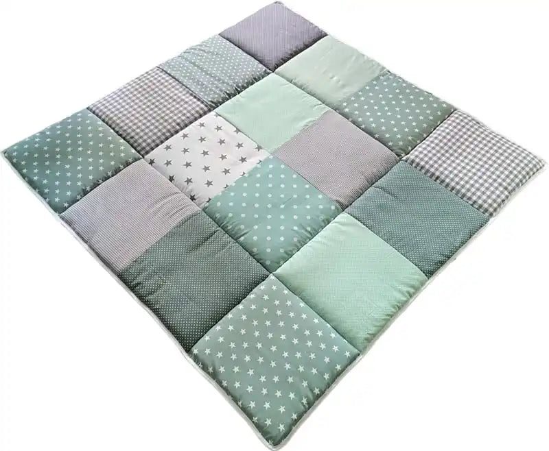 Een gestikte patchworkbaby-speelmat in verschillende tinten groen en grijs, met patronen zoals sterren, stippen en ruitjes.