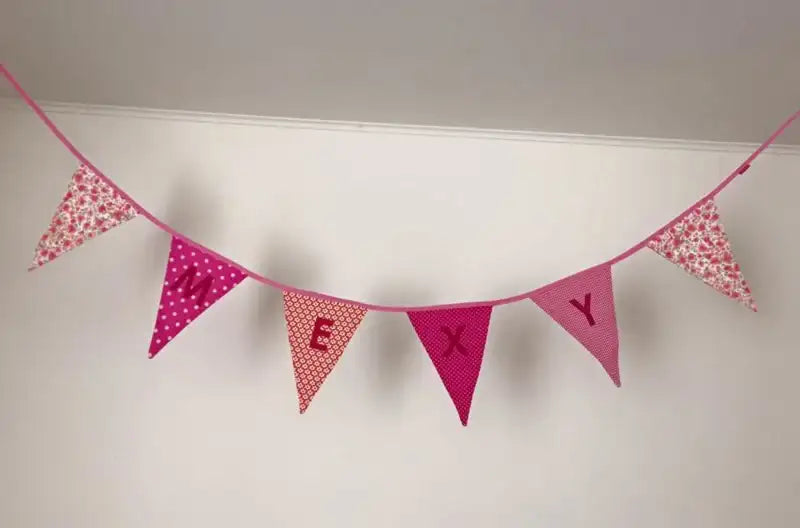 Roze bloemmotief stof banier met letters 'e x y' op elke vlag, hangend tegen een witte muur.