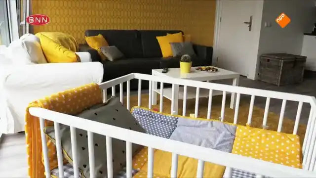 Een witte houten babywieg met gele en grijze beddengoed.