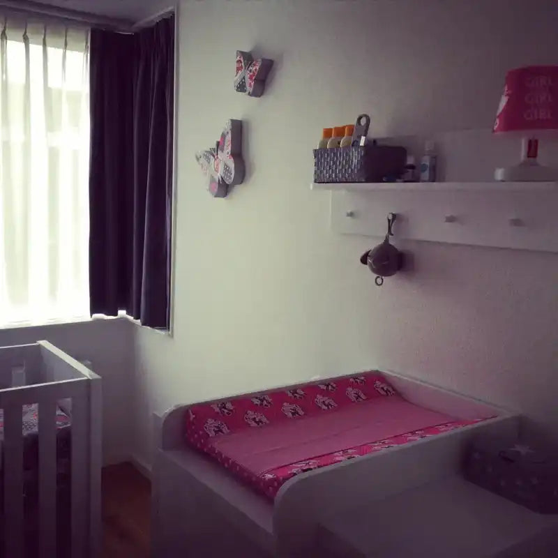 Een witte wieg met een roze verschoningskussen.